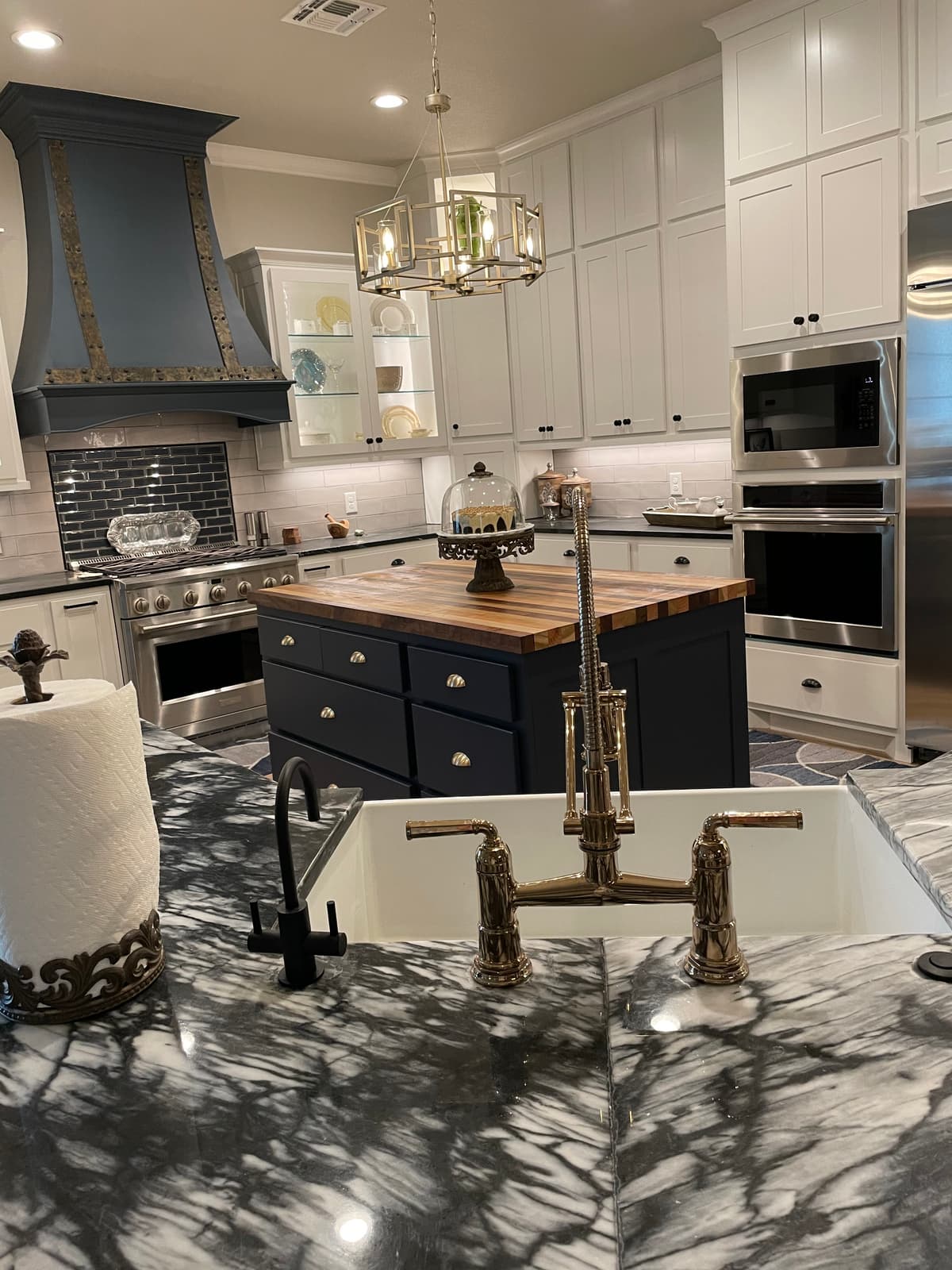 Custom navy kitchen island with butcher-block counter, brushed-gold pot filler, and veined marble by L&M Custom Designs and Build in Dallas Fort Worth